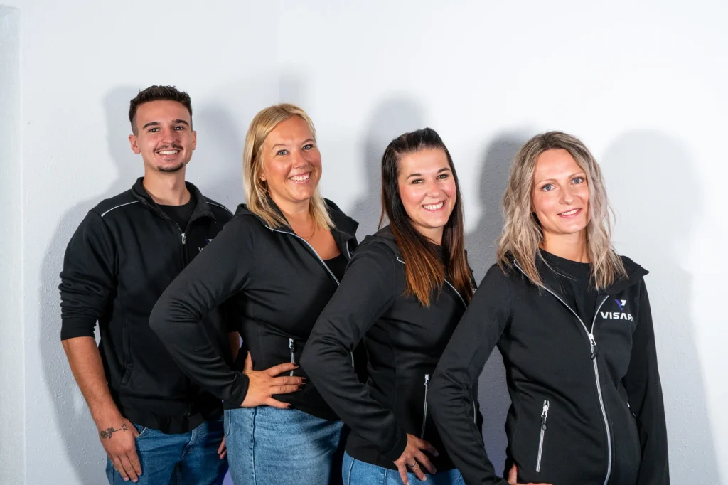 Vier Personen des VISARO Teams in Firmenjacken vor einer hellen Wand