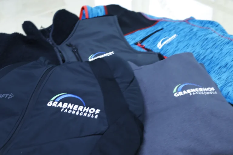 Gestapelte bestickte Jacken und Shirts einer Schulausstattung