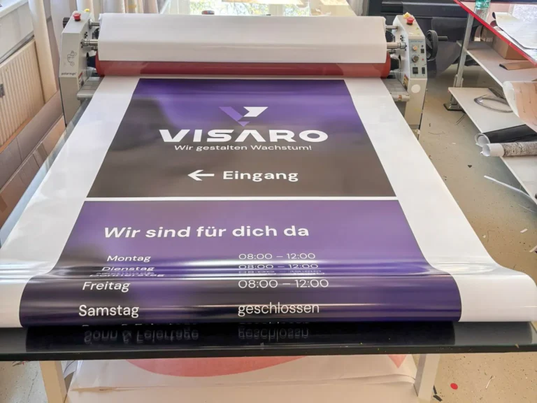 Frisch gedrucktes VISARO Banner mit Öffnungszeiten auf dem Arbeitstisch