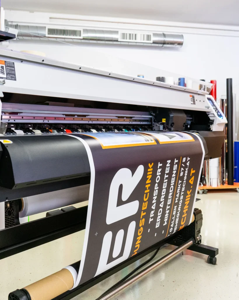 Großformatdrucker druckt ein Banner in Schwarz, Weiß und Orange