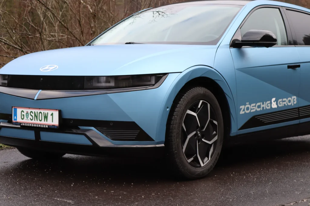 Hellblau foliertes Elektroauto mit Schriftzug an der Seite, schräg von vorne