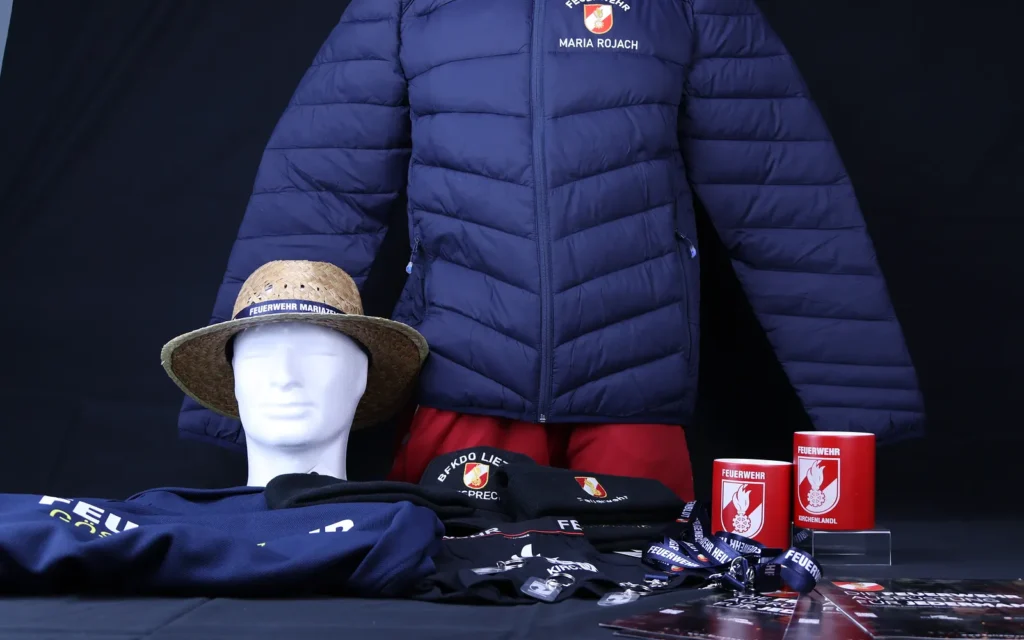 Steppjacke „Maria Rojach“, Strohhut, bestickte Hauben, Lanyards und rote Becher mit Feuerwehrwappen