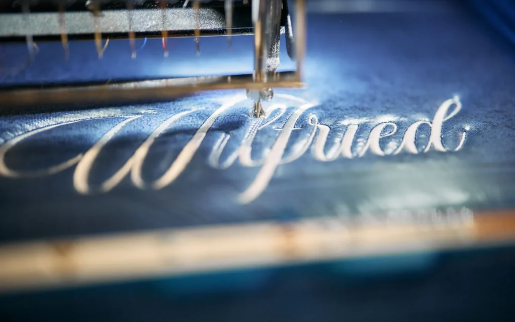 Gestickter Schriftzug in Schreibschrift unter der Stickmaschine