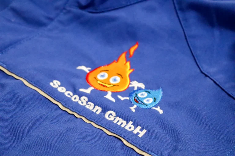 Gesticktes Firmenmaskottchen mit Schriftzug auf einem blauen Poloshirt